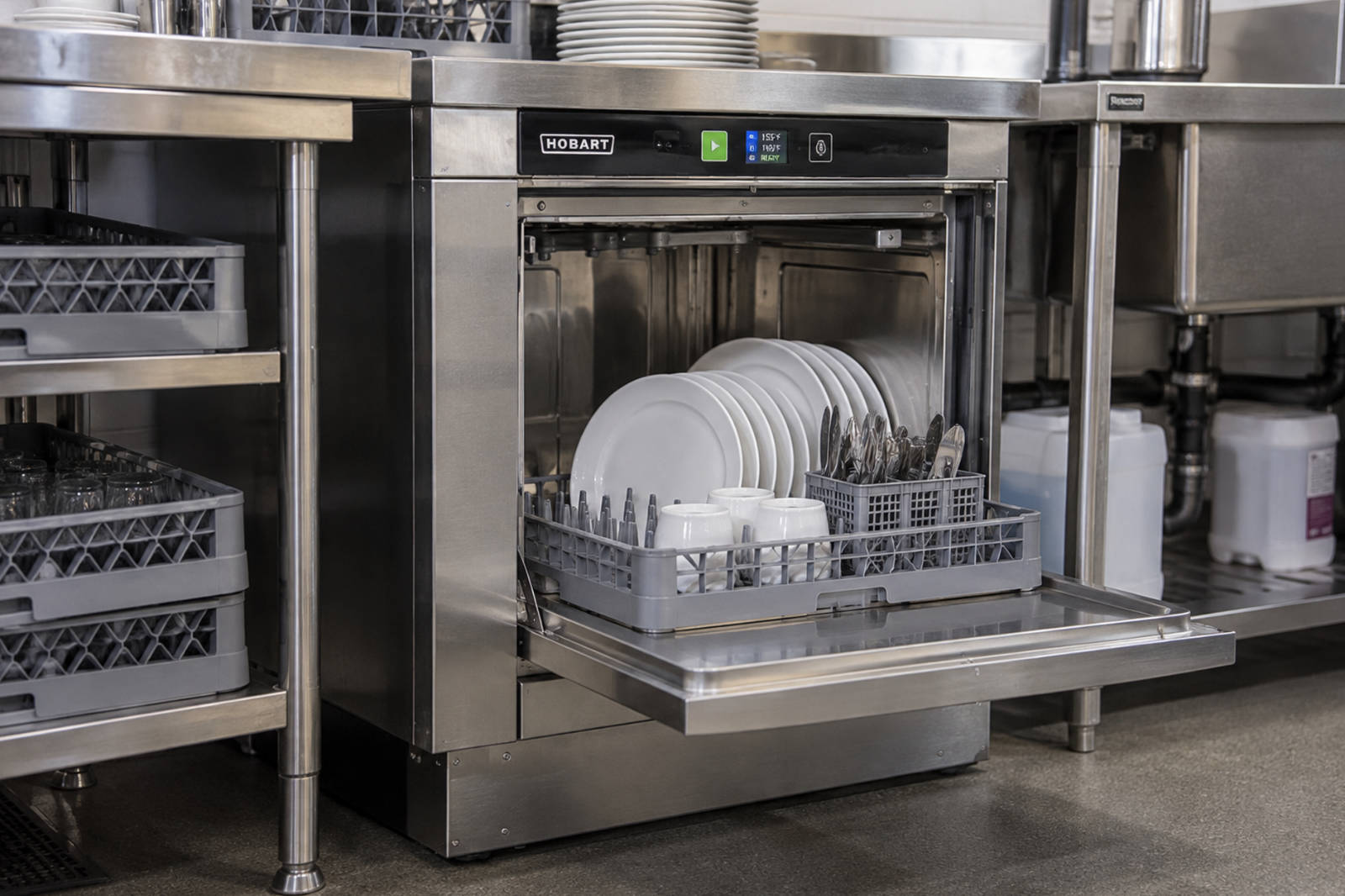 Stainless steel undercounter commercial dishwasher with its door open, loaded with clean white plates and coffee cups.
